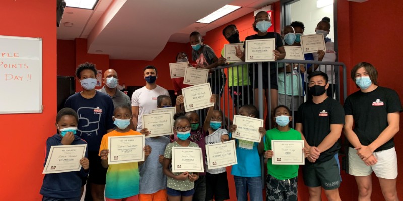 A couple of children wearing masks and holding up Hit the Books certificates