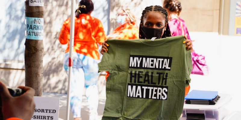 A woman in a mask holding up a green shirt that says "my mental health matters"