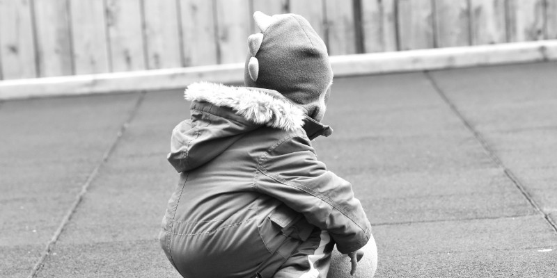 A child squatting down with a ball.