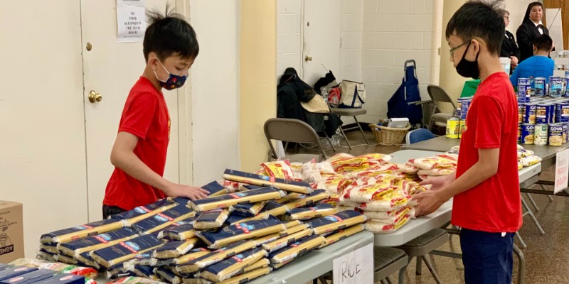 Two children help stock a table of pasta and rice bags