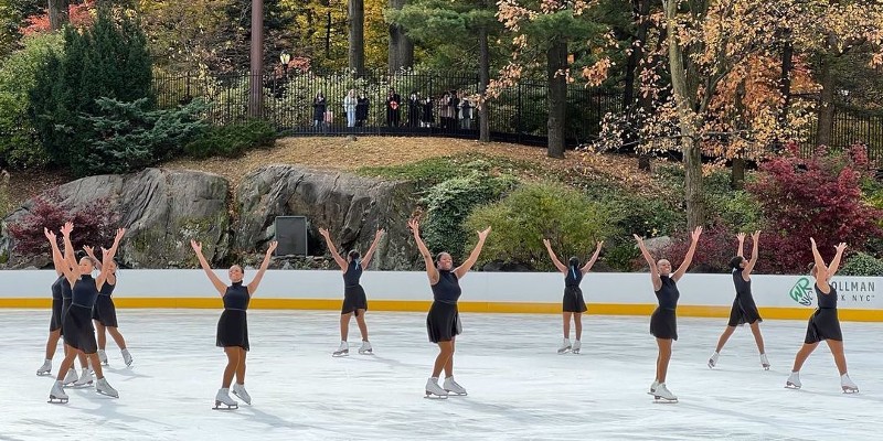 A group of people figure skating on a rink outside