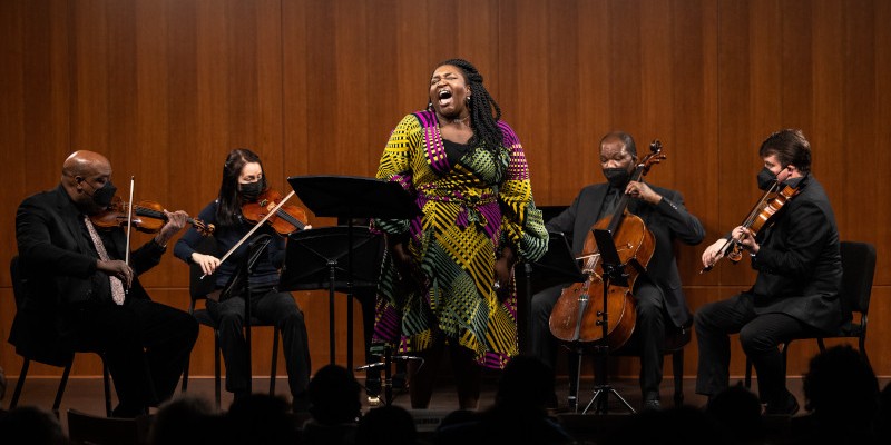 A woman singing in front of musicians playing string instruments