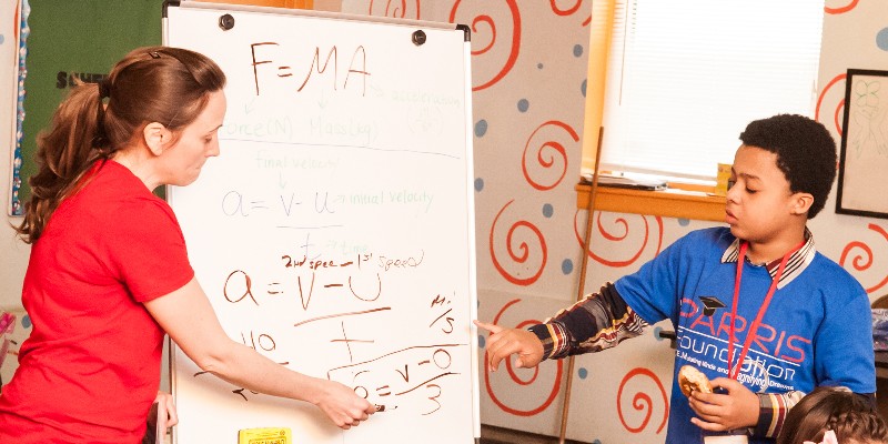A woman shows a formula to a boy on a white board.
