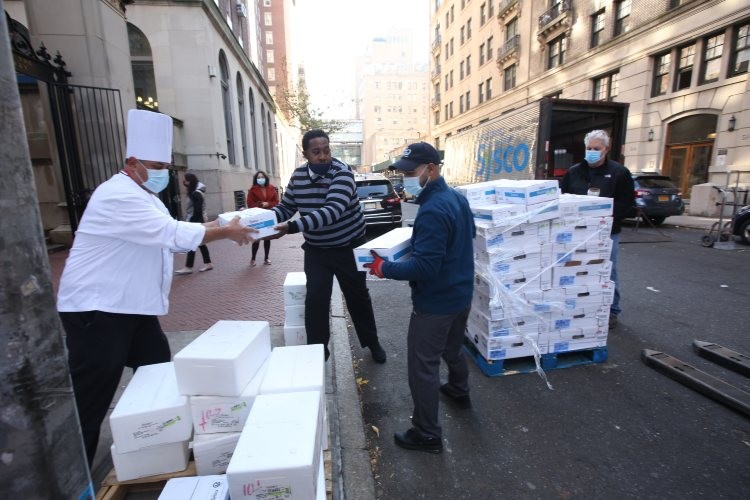 A man in a chef hat passes boxes to two other men wearing masks.