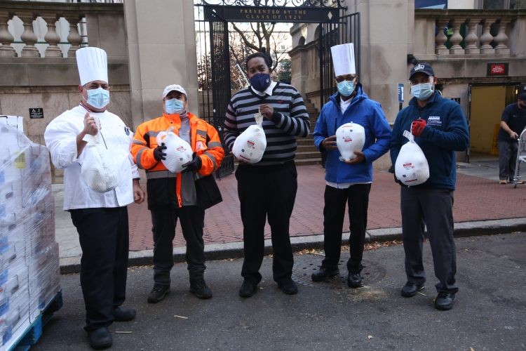 Five people in masks display the frozen turkeys in bags to the camera.