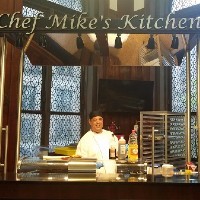 Chef Mike in an open kitchen with "Chef Mike's Kitchen" signage above it