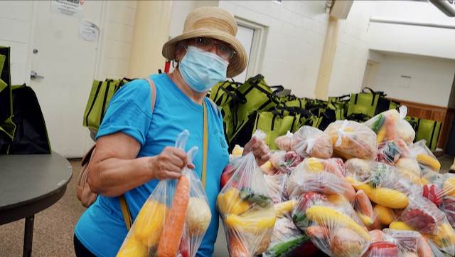 A food pantry patron stands in front of a table full of bagged vegetables.