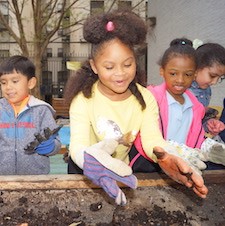 A girl in a yellow shirt and gloves plays with dirt.