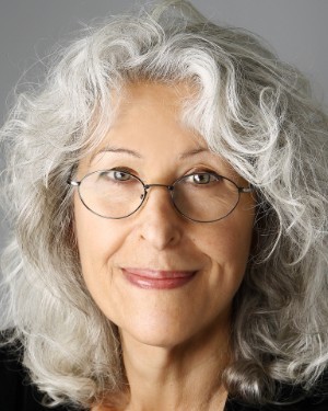 A headshot of a woman with white hair and glasses.