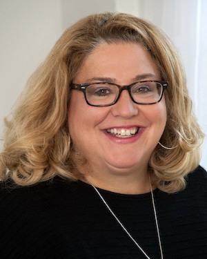 A headshot of a blonde woman wearing glasses.