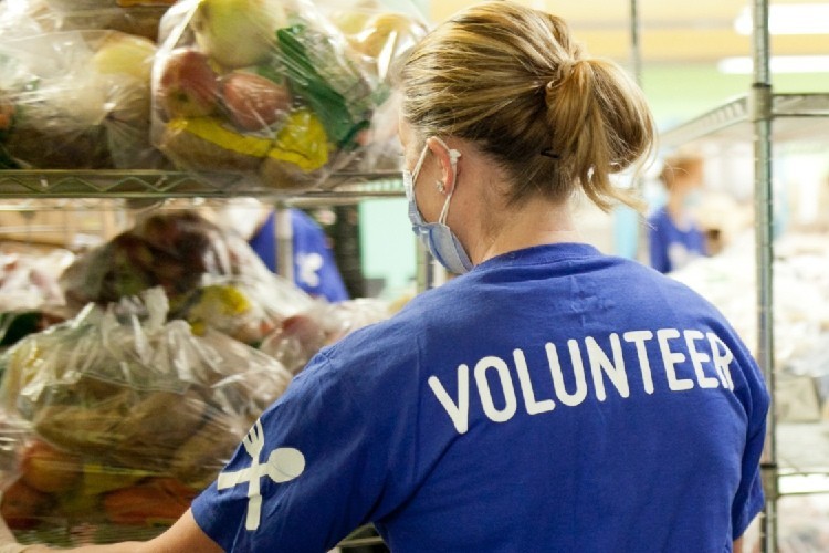 Back of person facing bags of food, their shirt says volunteer.