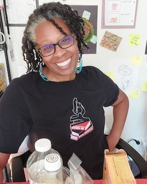 A woman with graying hair wearing glasses stands behind a science experiment