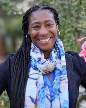 A headshot of a woman with her hair in braids wearing a scarf.