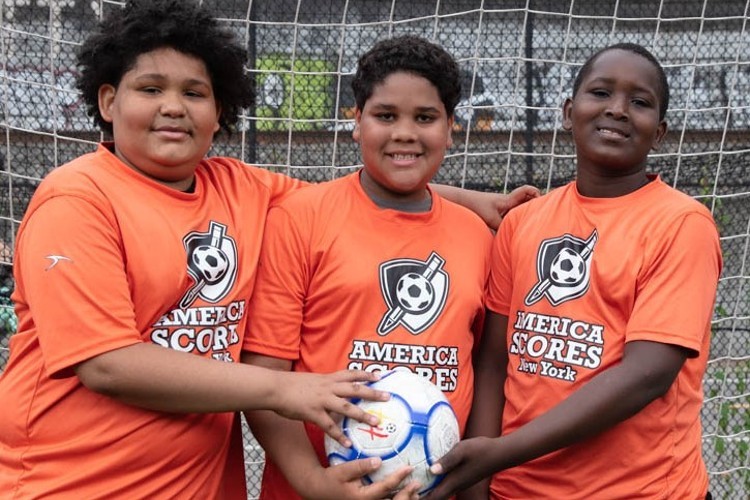 Three boys in orange shirts holding a soccer ball.
