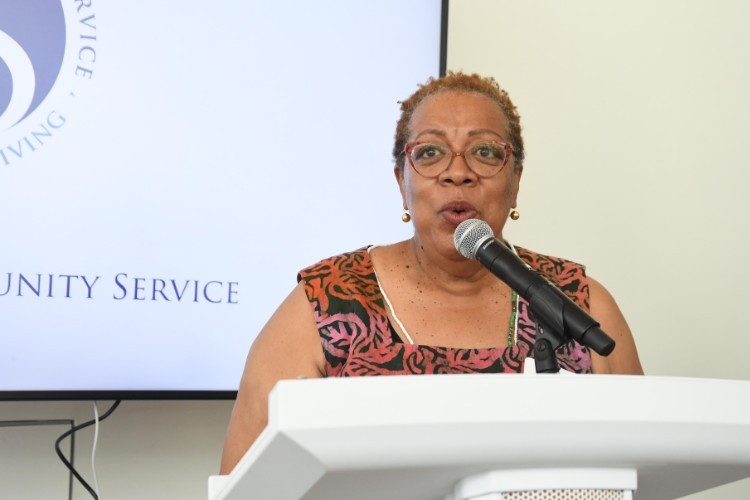 Photo by Eileen Barroso. A woman with short hair in glasses speaks into a microphone
