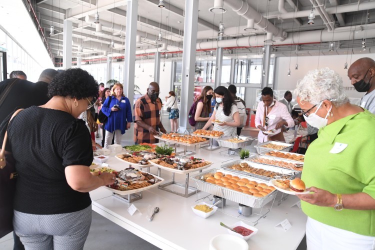 A group of people standing around a buffet taking food