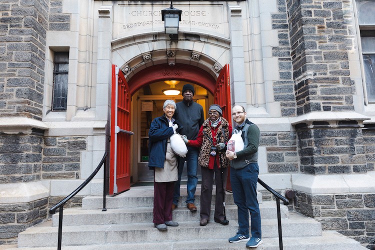 A group of four people standing in front of Broadway Presbyterian Church. 2 of them are holding packaged raw turkeys.