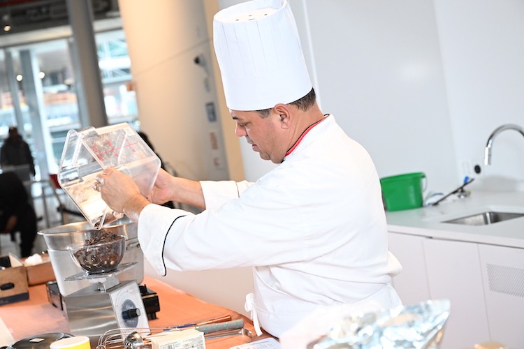 A man in a chef hat pours chocolate into a bowl.