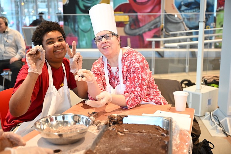 A woman in a chef had and young man in an apron show off their truffles for the camera.