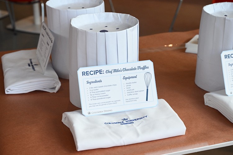 A card that says "Recipe: Chef Mike's Chocolate Truffles" leaning against a white chef's hat. The card lists the ingredients and equipment to make truffles.