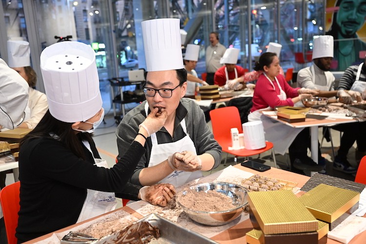 One person in a chef hat feeds another person in a chef hat a truffle.