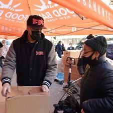 A man in a mask and coat hands a large cardboard box to a woman.