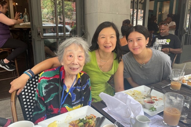Three women of different ages sitting at an outdoor table at a restaurant smiling at the camera.