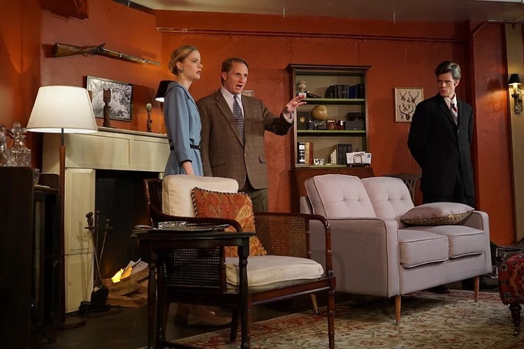 Three people standing in a furnished room performing a play