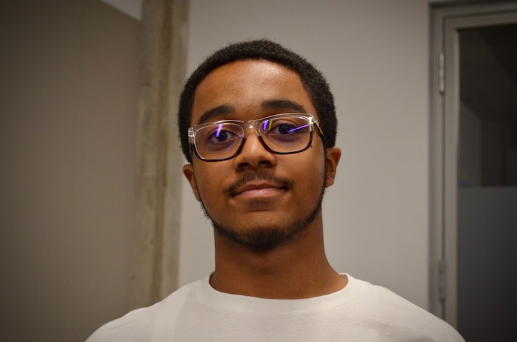 A young man in glasses and a white shirt smiles at the camera.