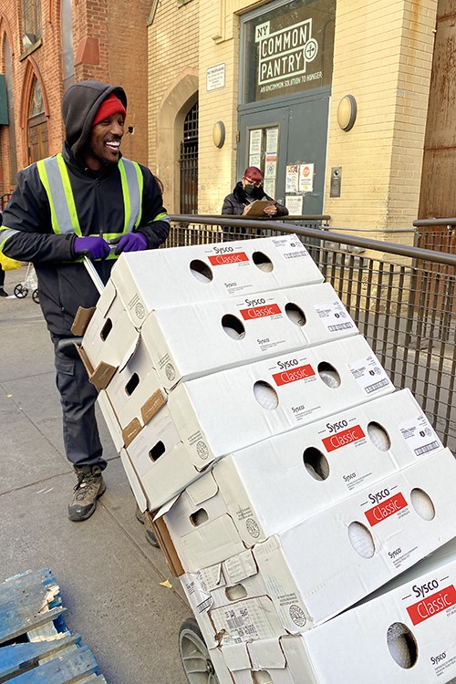 A man in a hoodie and reflective vest wheels a cart of Sysco boxes.