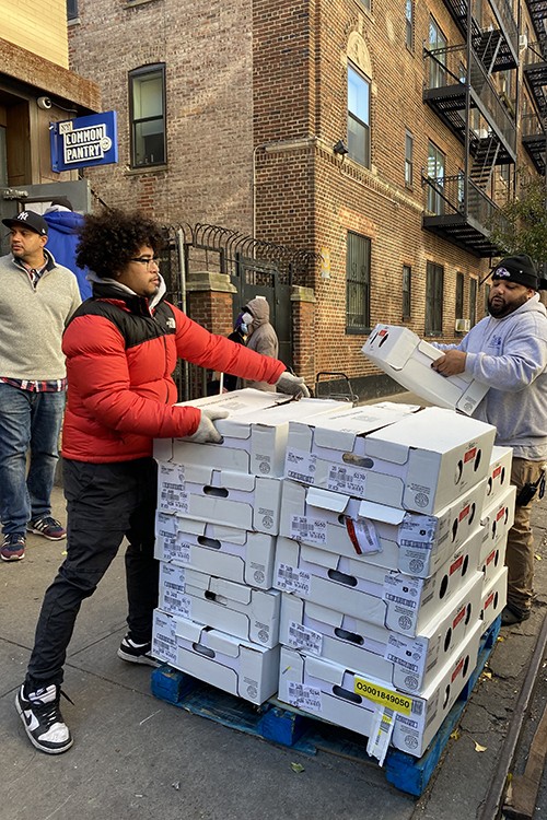 A man in a red coat and a man in a gray hoodie pick up boxes off a dolly.