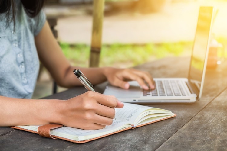 Person writing and typing on a laptop