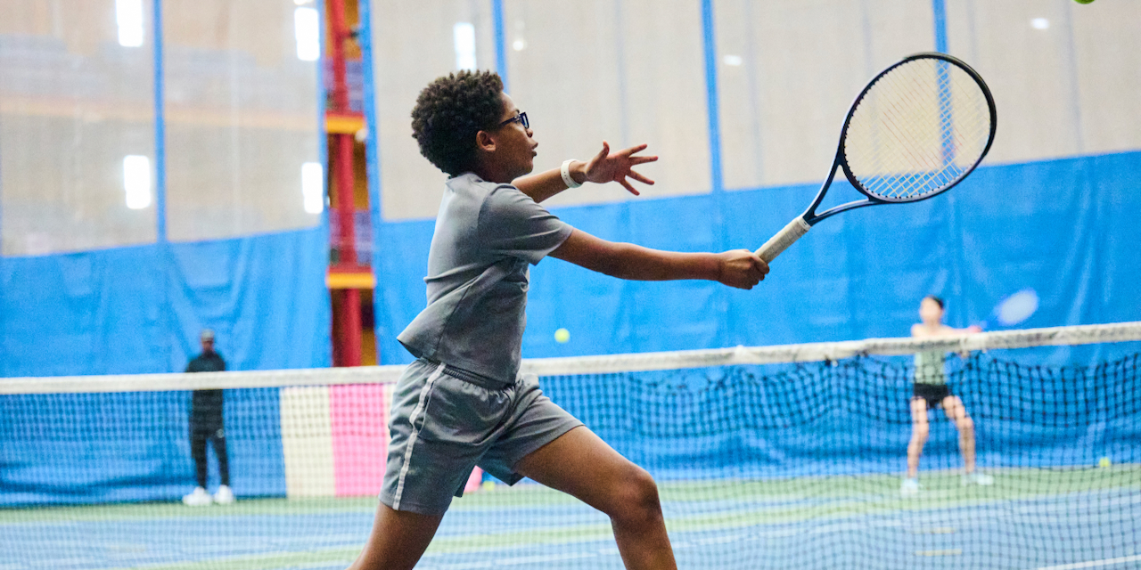 A young man in glasses runs with a tennis racket.