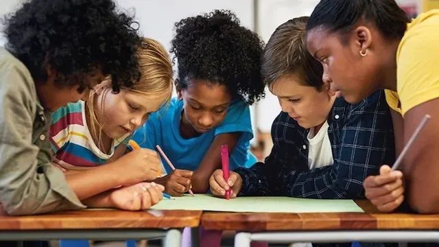 Young students huddle together working on a math problem.