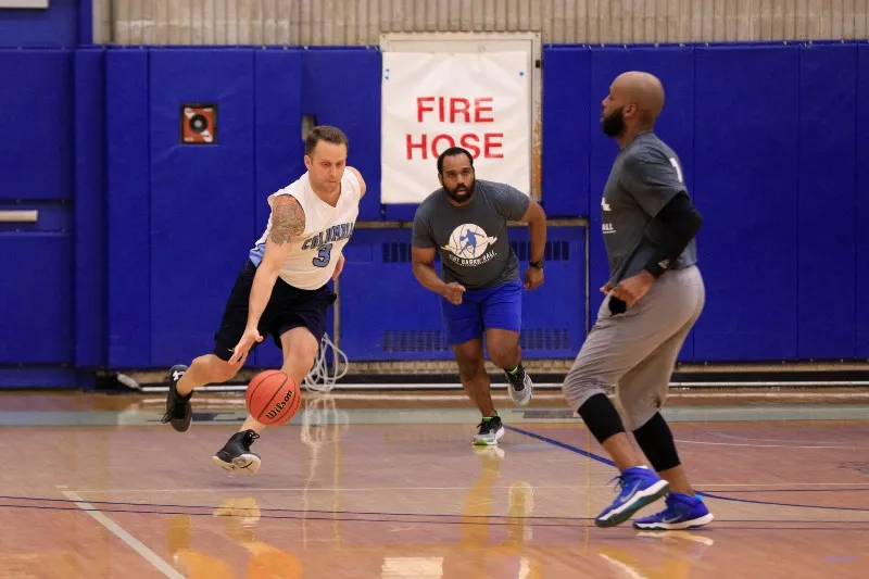 Three men playing basketball, with one dribbling past another.