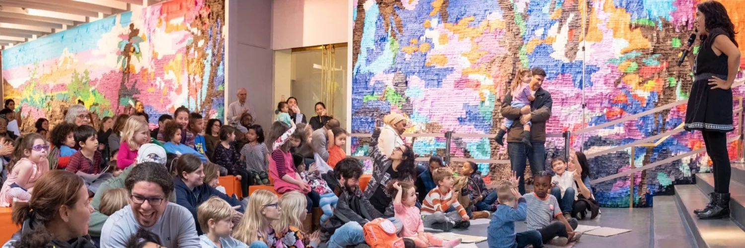 Photo of woman speaking to group of parents with their children for story time.