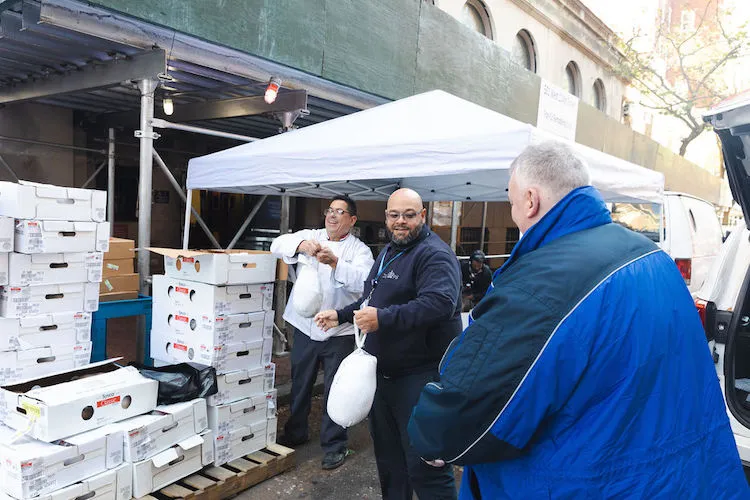 Three men passing bagged turkeys out of boxes.